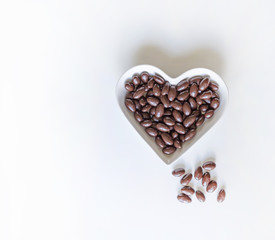 Nuts arranged in heart shape on background. Food image close up candy, chocolate milk, extra dark almond nuts. Love Texture on white grey table top view