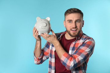 Happy young man with piggy bank and space for text on color background. Money saving