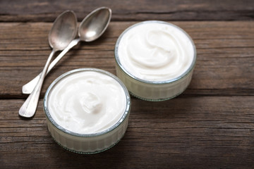 Fototapeta na wymiar Two glass bowls with white yogurt on old wooden desk.