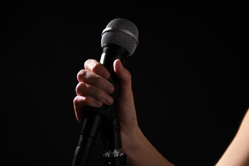 Woman holding microphone on black background, closeup