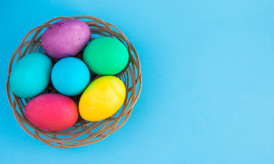 Colorful easter eggs in a basket on a blue color background with a copyspace