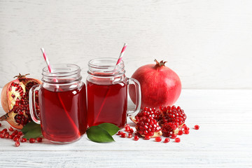 Mason jars of pomegranate juice and fresh fruits on wooden table, space for text