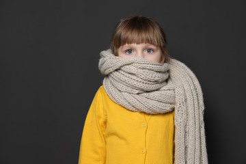 Funny little girl wrapped in scarf against dark  background, space for text. Cough precaution