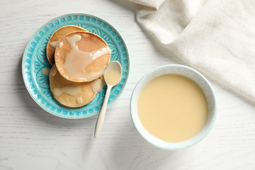 Bowl of condensed milk and pancakes served on wooden table, top view. Dairy products