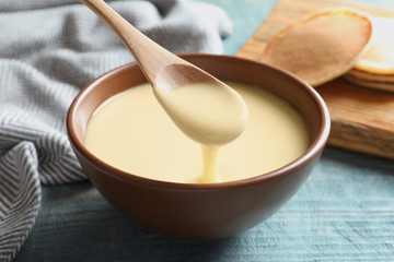 Fototapeta na wymiar Spoon of pouring condensed milk over bowl on table, closeup. Dairy products