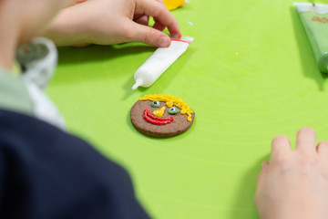 Praca plastyczna zrobiona przez dziecko. Cynamonowe okrągłe ciastko udekorowane przez dziecko. Uśmiechnięta buzia namalowana kolorowymi lukrowymi pisakami. © Tomasz
