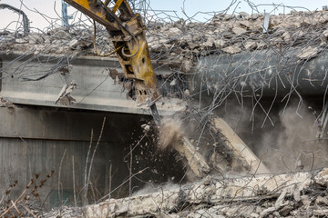 Professional demolition of reinforced concrete structures using industrial hydraulic hammer. Rods of metal fittings. Wreckage and crumbles of concrete.