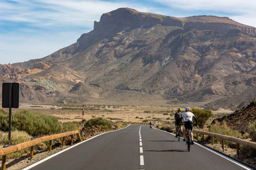 Cyclist cycling on a road through volcanic landscape.