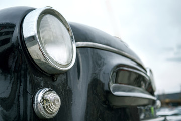 Fragment of an old black car. Chromium-plated headlight and flashlight. Selective focus. Outdoors.