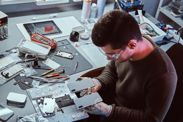 Electronic technician holds two identical smartphones for comparison, in one hand broken and in...
