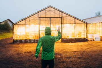 the greenhouse glows with yellow light in the supper. The guy is near the greenhouse