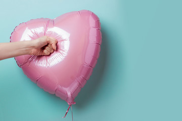 Female hand punching a heart-shaped balloon © Orlovskaya