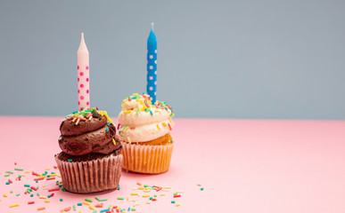 Two birthday cupcakes with candles on blue and pink pastel background, copy space.