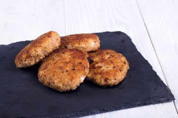 cutlets on a black flat plate, on a white wooden background