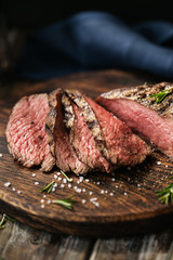 Juicy medium Beef Rib Eye steak slices on wooden board with herbs spices and salt.