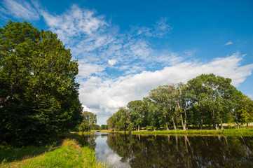 Beautiful still lake with trees on the horizon and white puffy clouds in the sky. Peaceful summer...