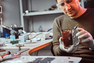 Electronic technician showing a modern smartphone with a broken body in a repair shop