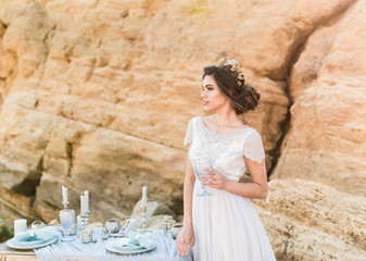 Attractive brunette bride in light chiffon wedding dress embroidered with beads posing near the...