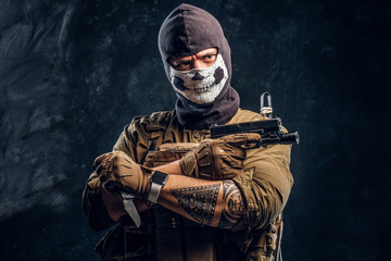 A terrorist in a military uniform and a skull balaclava holding a pistol and a knife and looks at...