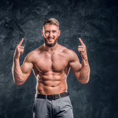 Cheerful shirtless man with the muscular body posing for a camera. Studio photo against dark wall background