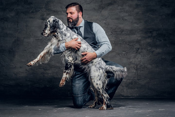Middle-aged hunter dressed in elegant clothes sits on his knee and holding his purebred English...