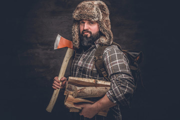Brutal woodcutter with firewood and ax. Studio photo against a dark textured wall