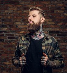 Confident bearded guy with tattoos on his hands and neck in the military shirt. Studio photo...