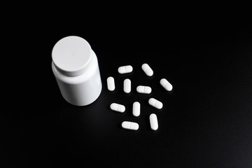 White pills, tablets and white bottle on black background.