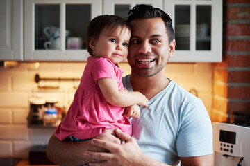 Smiling father holding baby girl in kitchen at home