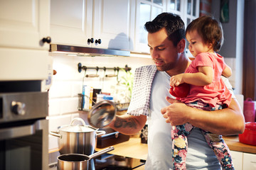 Father preparing meal and holding baby girl in kitchen at home