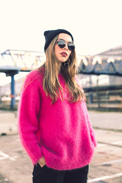 Portrait of fashionable young woman wearing sunglasses, cap and pink knit pullover