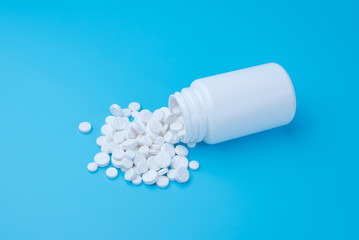 Medicine white pills or tablets drop out of the white bottle on blue background