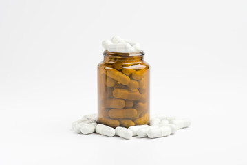 Medicine white pills or tablets drop out of the brown glass bottle on white background.