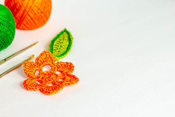 crocheted bright colorful elements (orange flower and green leaf) closeup, white background, copy space