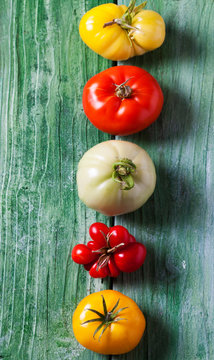 Row of five different tomatoes on green wood