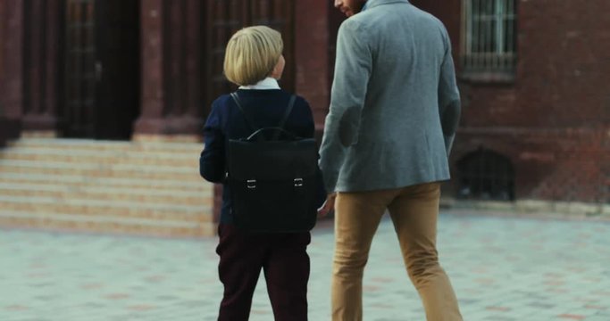 Back view on the caucasian father walking with his son when bringing him to school in the morning. Rear.