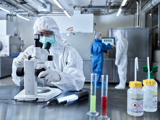 Chemists working in industrial laboratory, wearing protective clothing, using microscope