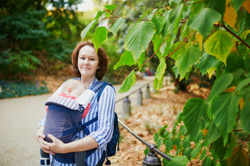 Happy young woman with her baby in carrier