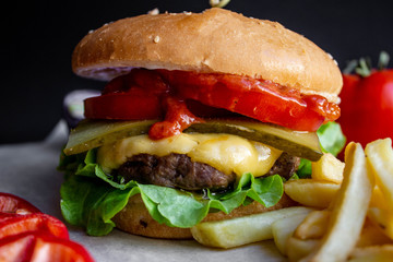 fresh tasty cheese burger with french fries and vegetables on black background