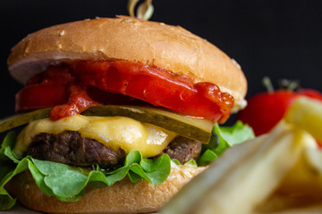 fresh tasty cheese burger with french fries and vegetables on black background