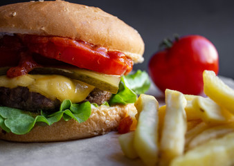 fresh tasty cheese burger with french fries and vegetables on black background
