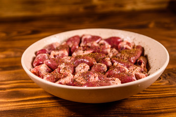 Ceramic plate with raw chicken hearts on wooden table