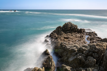 Long exposure of deep blue water, swirling surf, and rocky cliffs of central California