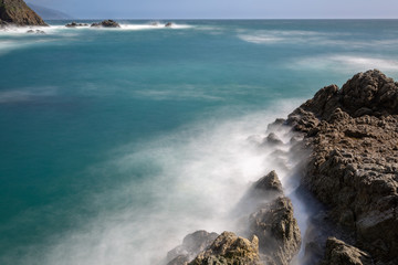 Fototapeta premium Long exposure of deep blue water, swirling surf, and rocky cliffs of central California