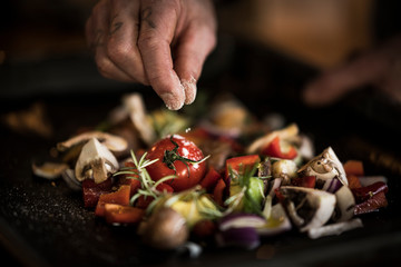 Hand seasoning vegetables on a baking tray