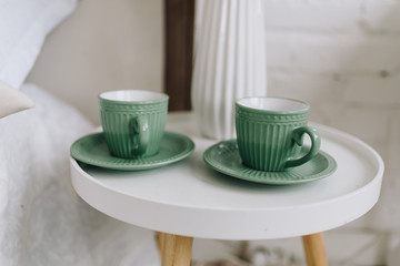 Two cups with saucers on a modern nightstand or bedside table. Coffee cups.