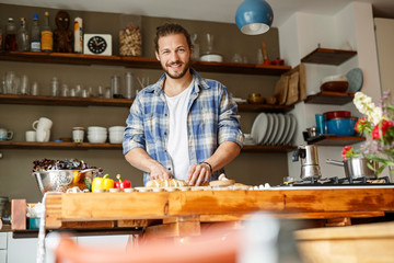 Young man preparing food at home, slicing bread