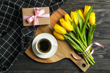 Beautiful tulips, cup of coffee, present and towel on wooden background