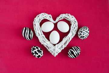 Easter eggs painted like zebra, cow, snow leopard. Three white eggs inside a white heart on red background. Top view.
