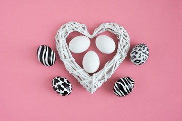 Easter eggs painted like zebra, cow, snow leopard. Three white eggs inside a white heart on pink background. Top view.